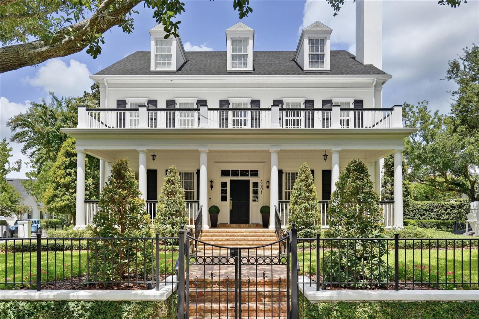A striking front elevation showcases the home’s symmetrical design, expansive covered porch, upper balcony and beautifully manicured landscaping. — 4601 New Broad Street, Orlando, Florida